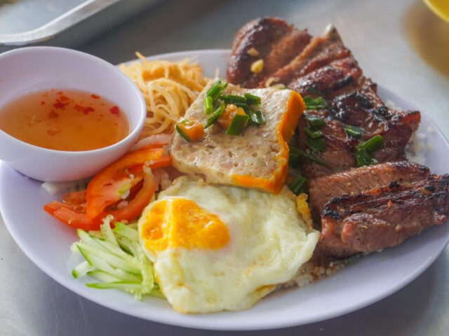 Mâm cơm tấm với sườn nướng, trứng ốp la, và rau sống trên đĩa