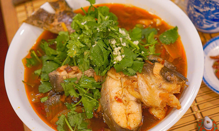 Nồi canh cá chua cay Quý Châu nóng hổi bốc khói, với cá tươi, rau củ và nước dùng đỏ cam hấp dẫn, đặc trưng của ẩm thực dân tộc Miêu.