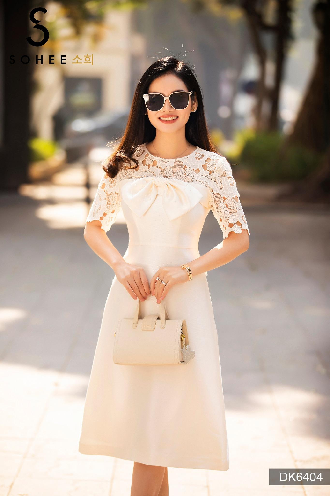 Phụ nữ mặc váy đen dáng ôm nhẹ, cổ áo sơ mi trắng, áo vest ngoài họa tiết kẻ caro